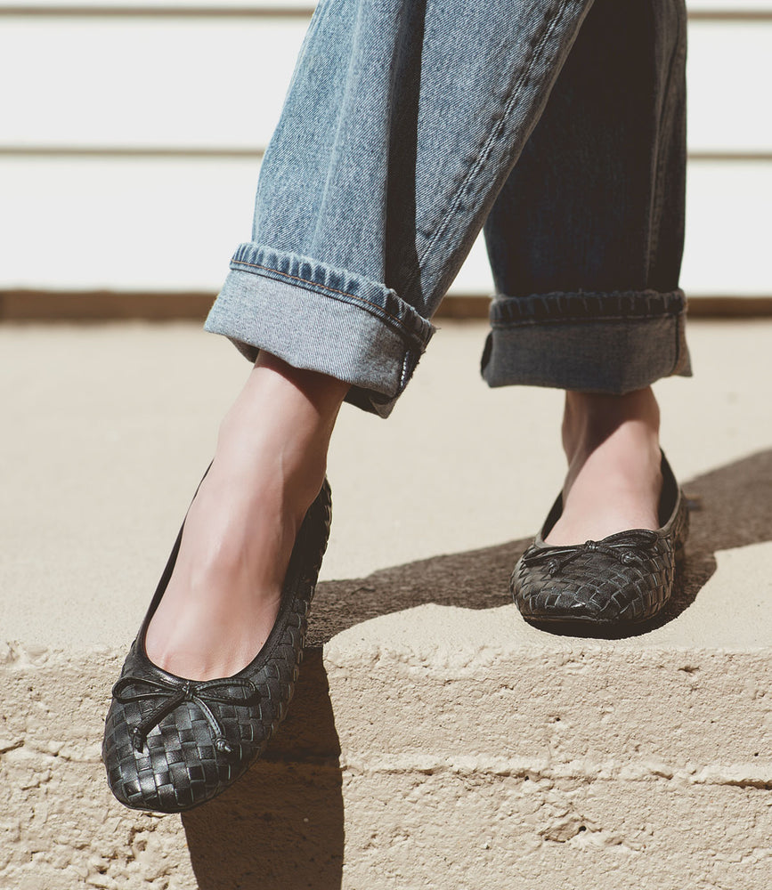 
                  
                    Person wearing rolled-up jeans and Roan's Business black hand-woven leather flats, standing on a concrete step.
                  
                