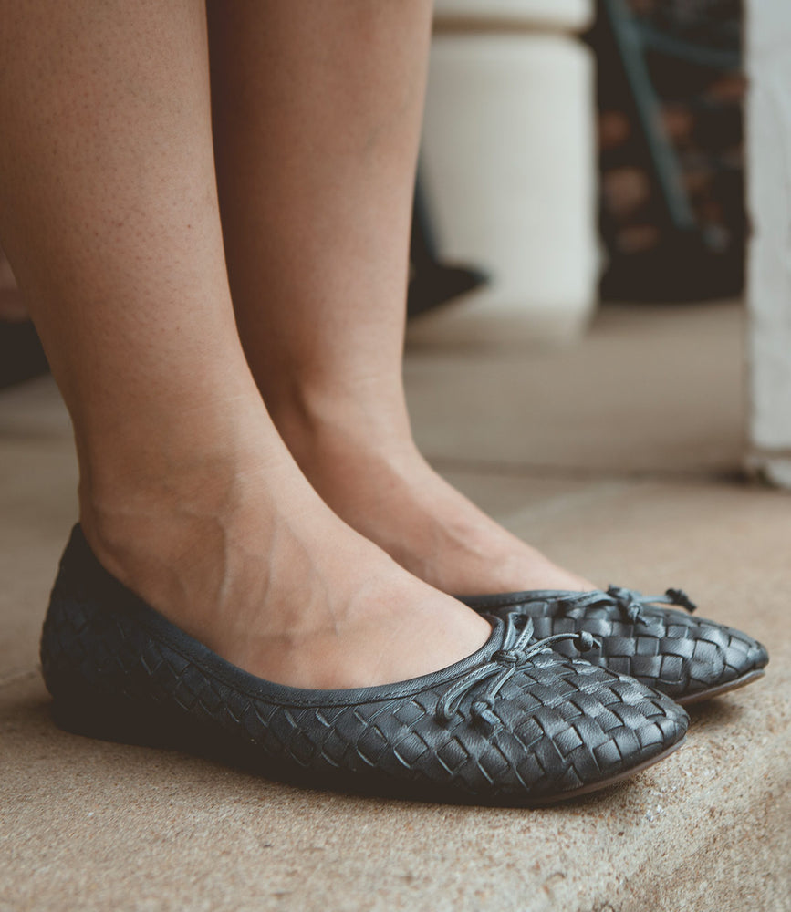 A pair of feet wearing black Roan Business slip-on ballerina shoes, showcasing intentional craftsmanship.