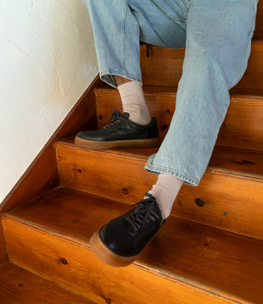 
                  
                    Person sitting on wooden stairs wearing blue Eminent jeans, beige socks, and sleek Roan lace-up sneakers with a comfortable insole.
                  
                