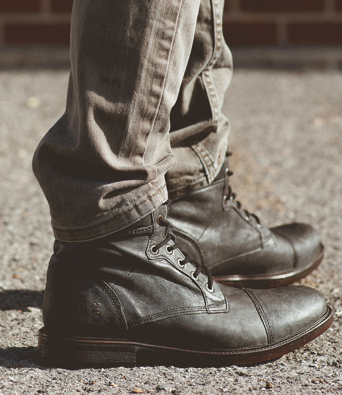 
                  
                    A person wearing Roan's Lecture dark brown men's leather boots with a padded collar and cuffed beige pants stands on a concrete surface.
                  
                