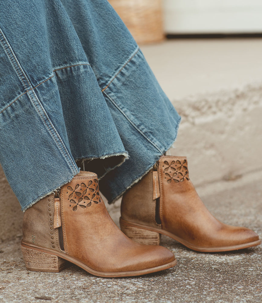 
                  
                    A person wearing a long denim skirt and Liz Cutout brown leather ankle boots by Roan, featuring a unique cutout petal design, stands on a textured stone surface, showcasing the beauty of mixed materials.
                  
                