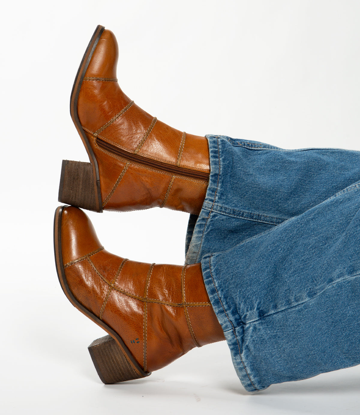 
                  
                    Roan's "Often" ankle boots in red-brown leather, showcasing intricate piping and side zippers with medium block heels, are stylishly matched with blue denim jeans on a white background.
                  
                