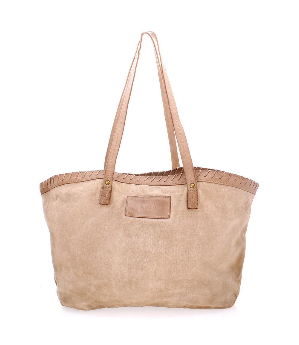 A versatile beige tote bag with leather handles and stitched trim, featuring a small rectangular label on the front. This classic Rutherford tote from Roan is perfect for everyday use.