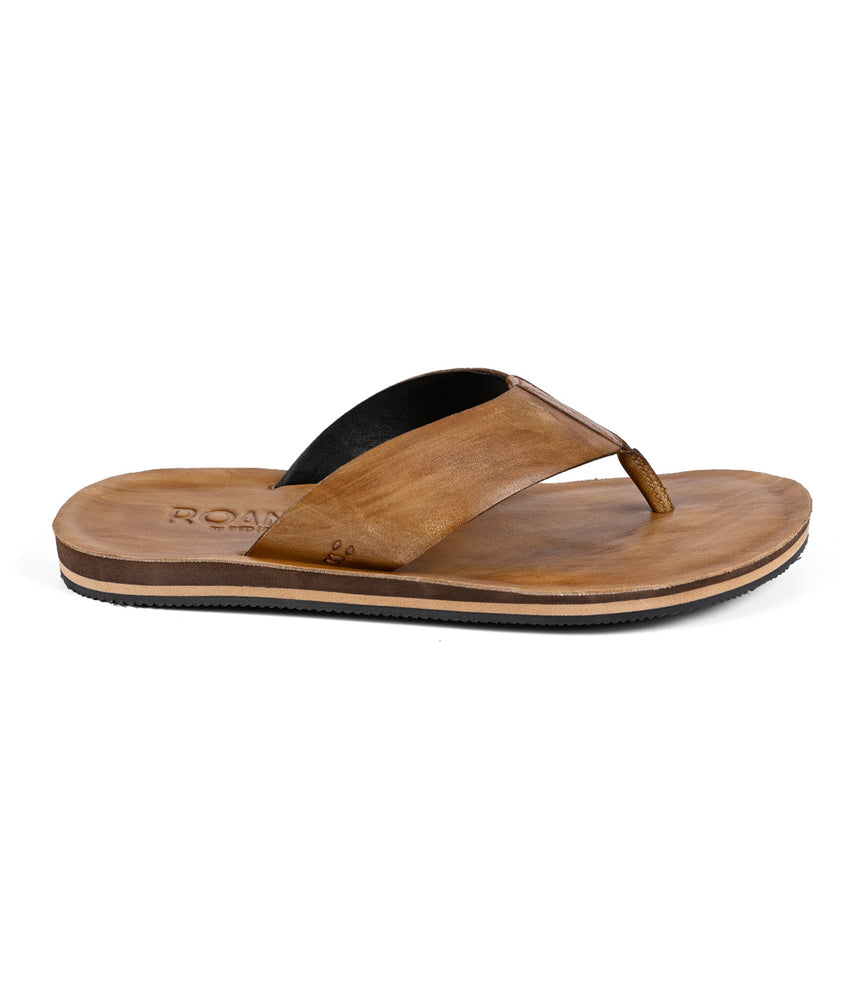 The Townfolk by Roan is a brown leather flip-flop sandal featuring a distressed strap, flat sole, and minimalist design, offering a touch of rustic charm.