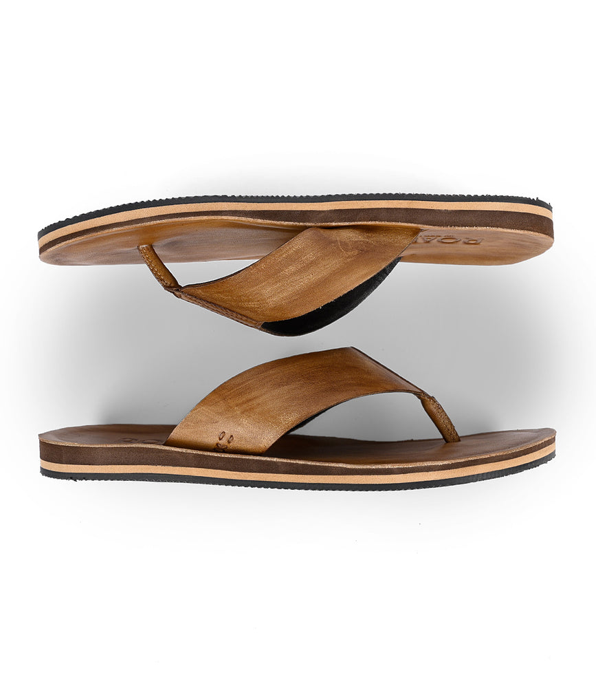 
                  
                    Two Townfolk flip-flops by Roan, featuring brown leather straps and black soles, exhibit rustic charm as they parallel each other on a plain white background from an overhead view.
                  
                