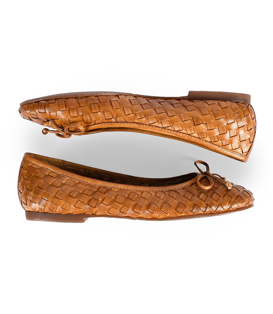 
                  
                    A pair of hand-woven leather Business by Roan slip-on ballerina shoes in brown, featuring small bows on the front, shown from the side.
                  
                