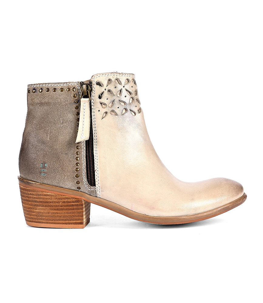 
                  
                    The Liz Cutout by Roan is a beige ankle boot featuring decorative cutouts, a side zipper, gold rivet details, and a chunky wooden heel.
                  
                