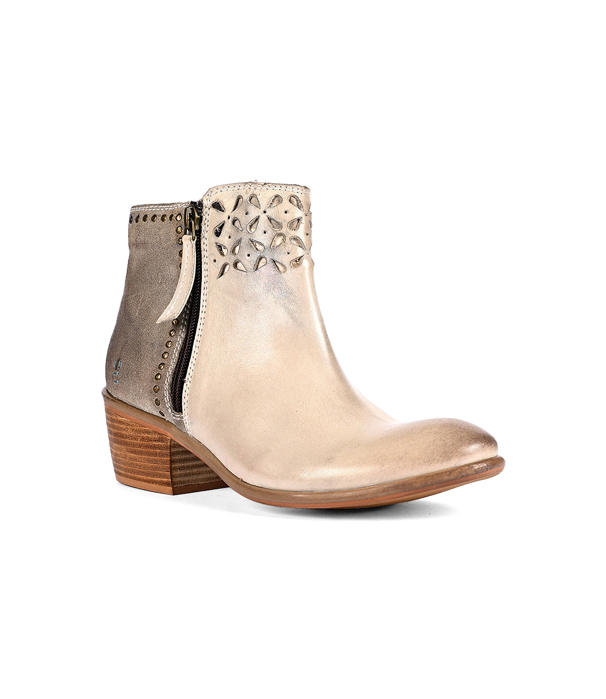 
                  
                    The Liz Cutout by Roan is a beige ankle boot featuring a low wooden heel, side zipper, and decorative perforations near the top with subtle gold rivet details.
                  
                