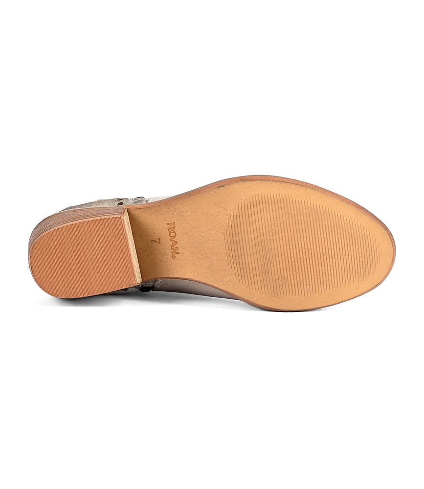 
                  
                    The image shows the bottom view of a beige Liz Cutout shoe from Roan. The rubber sole features a partially ridged texture and has the number "7" along with "ROAM" printed on it. The mixed materials design includes subtle gold rivet details adding a touch of elegance to its overall look.
                  
                