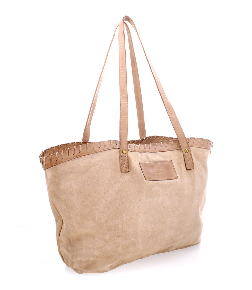 
                  
                    A beige tote bag crafted from cotton canvas with leather straps and refined decorative stitching along the top edge, exuding timelessness; introducing the Rutherford by Roan.
                  
                